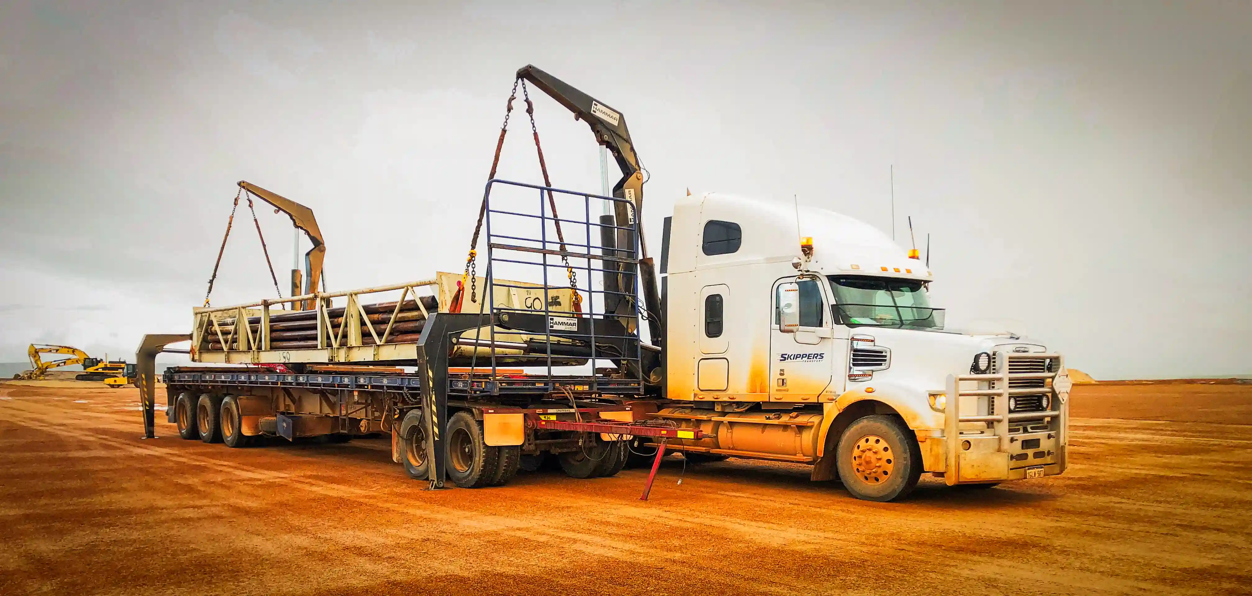 a picture of a Skippers Transport triple road train loaded with mine equipment parked on the side of the road up north in the evening as the sun sets